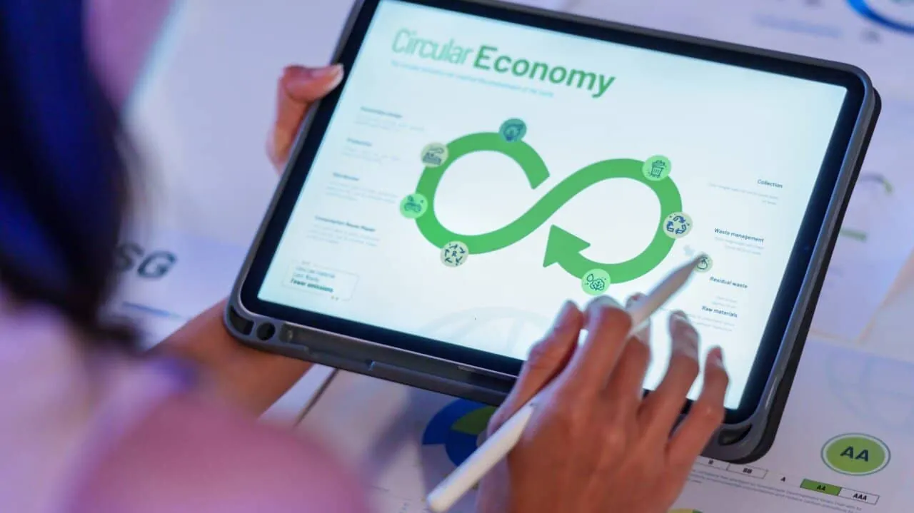 Hands with a stylus on a tablet showing a green infinity-loop "Circular Economy" diagram.