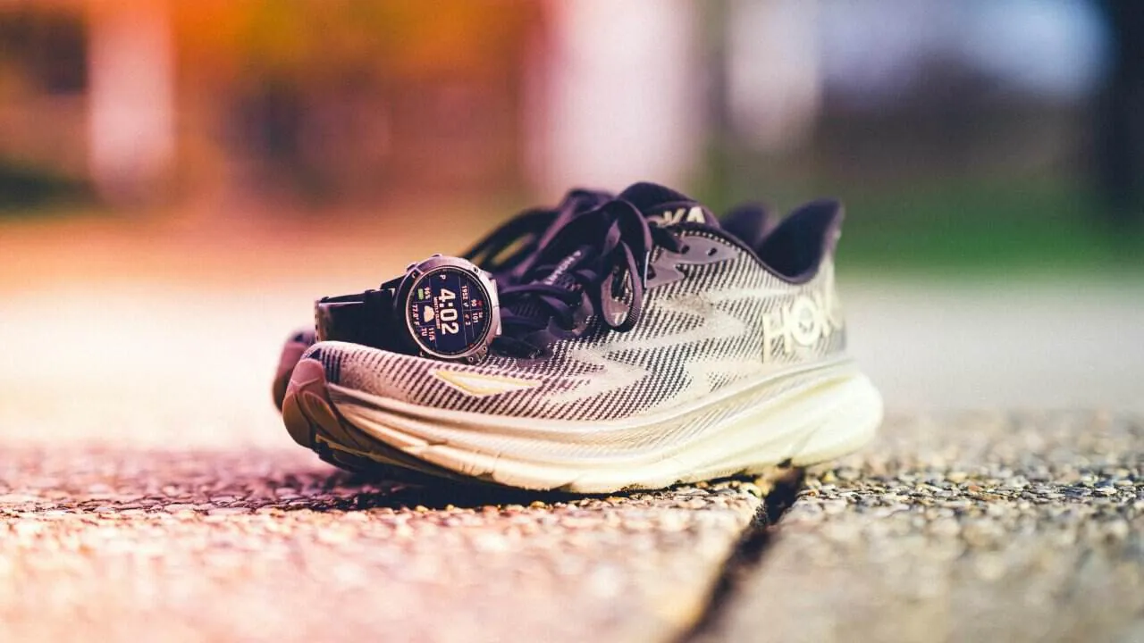 Hoka running shoe on pavement with a sport smartwatch resting on it, showing a time of 4:02.