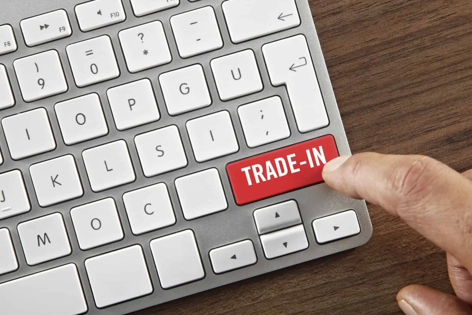 Finger pressing a red "Trade-In" key on a white computer keyboard.