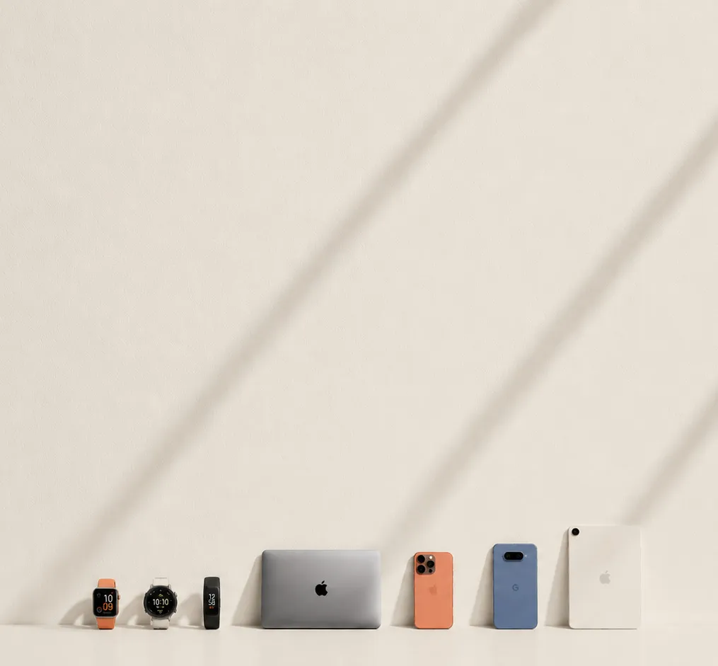 Smartwatches, a fitness band, a laptop, two phones and a tablet lined up against a cream wall.