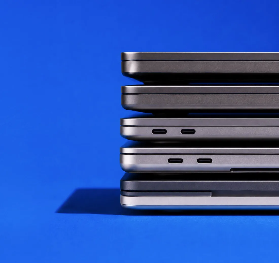 A stack of silver and space gray laptops, seen edge-on against a bright blue background.